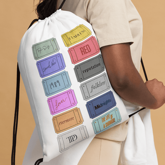 White drawstring bag with Taylor Swift colorful labels held by a person against a beige background