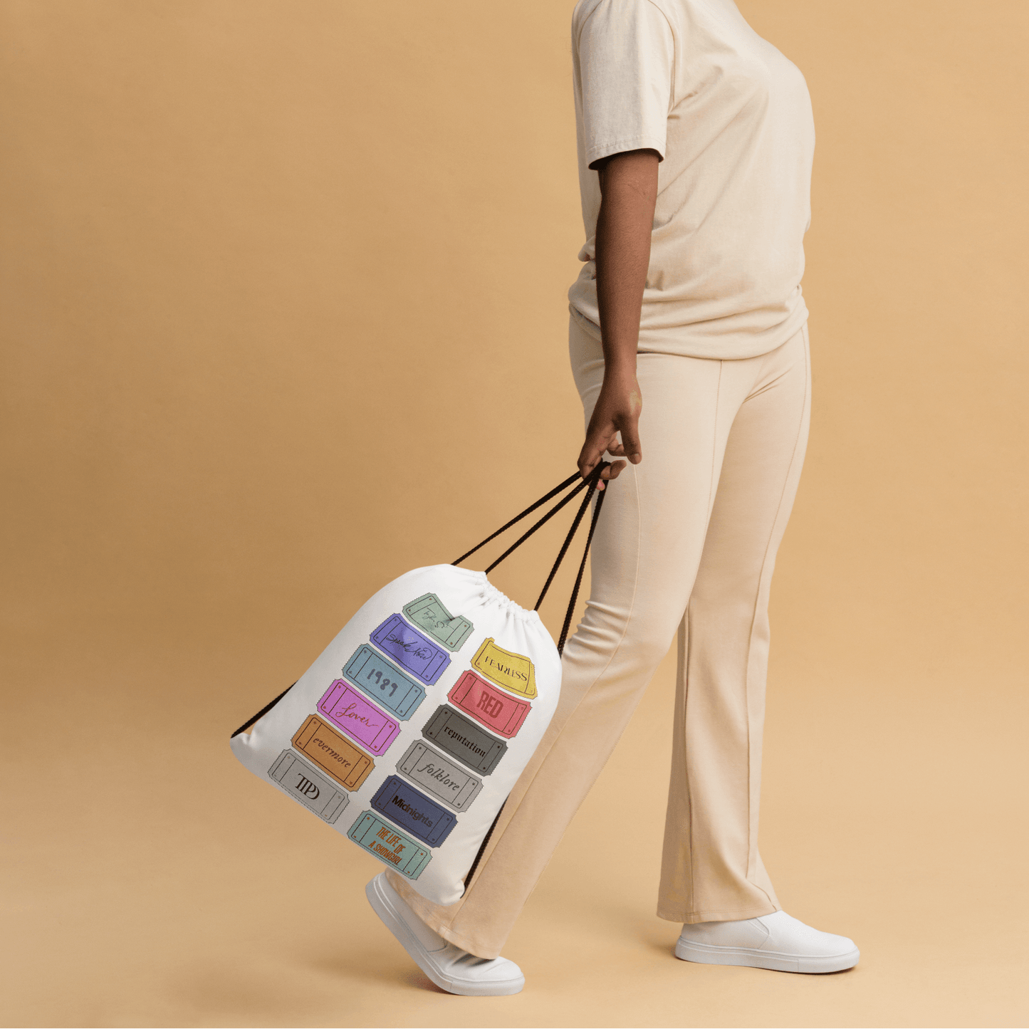 Woman holding a Taylor Swift 12 album tote bag with color swatches against a beige background