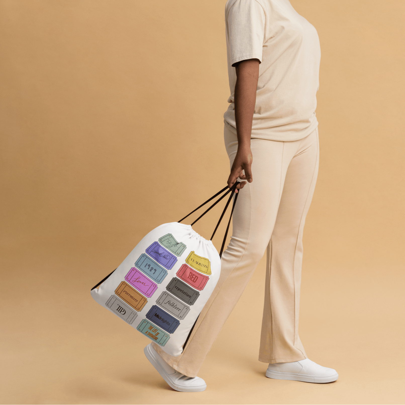 Woman holding a Taylor Swift 12 album tote bag with color swatches against a beige background